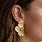 Boucle d'oreille en acier inoxydable doré, en forme de fleur avec des pétales texturés et un centre granuleux, portée sur une
