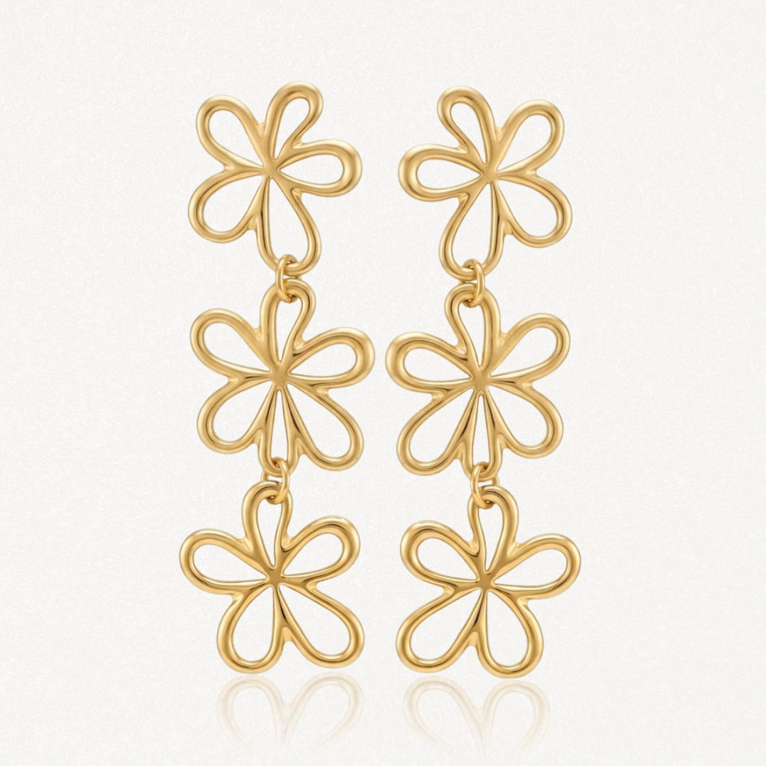 Boucles d'oreilles dorées pendantes, avec trois fleurs ajourées stylisées liées sur chaque boucle.