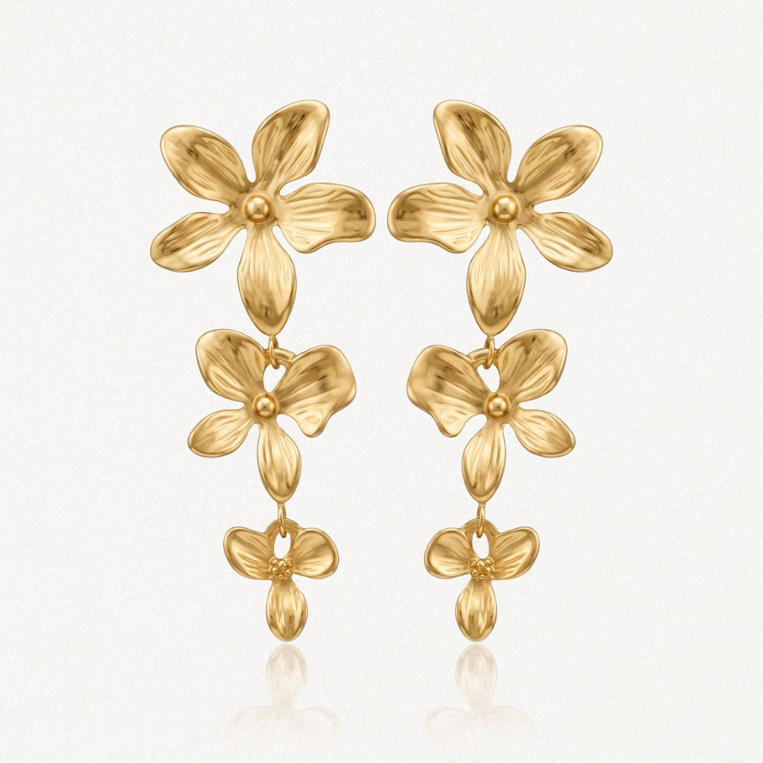 Paire de boucles d'oreilles dorées pendantes, composées de trois fleurs stylisées en relief de taille décroissante.