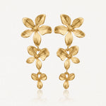 Paire de boucles d'oreilles dorées pendantes, composées de trois fleurs stylisées en relief de taille décroissante.