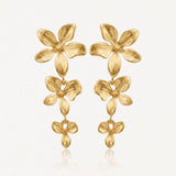 Paire de boucles d'oreilles dorées pendantes, composées de trois fleurs stylisées en relief de taille décroissante.