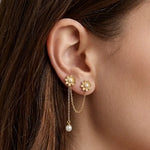 Boucles d'oreilles doubles en acier inoxydable doré, avec deux marguerites à perle blanche, reliées par des chaînes. Une