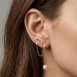 Double boucles d'oreilles en acier inoxydable doré, avec deux motifs de fleurs, une chaîne les relie et une perle pampille.