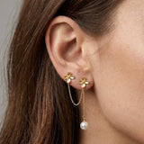 Double boucles d'oreilles en acier inoxydable doré, avec deux motifs de fleurs, une chaîne les relie et une perle pampille.