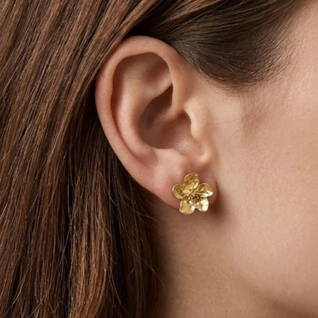Puce d'oreille fleur de cerisier en acier inoxydable doré, portée sur un lobe d'oreille. Fleur avec aspect texturé.