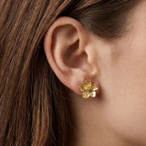 Puce d'oreille fleur de cerisier en acier inoxydable doré, portée sur un lobe d'oreille. Fleur avec aspect texturé.