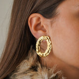 Boucle d'oreille ovale martelée au relief organique en acier inoxydable doré portée sur une oreille.