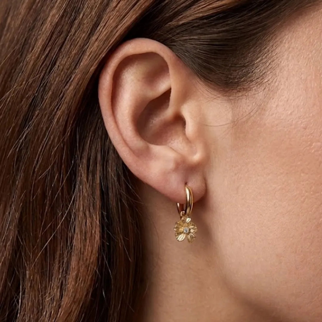 Boucle d'oreille mini créole en acier inoxydable dore avec un pendentif fleur texturé et un strass zirconium central sur une