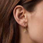Boucle d'oreille mini créole en acier inoxydable dore avec un pendentif fleur texturé et un strass zirconium central sur une