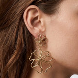Une double boucle d'oreille pendante en forme de fleurs originales, en acier inoxydable doré, portée sur l'oreille d'une