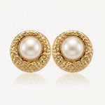 Paire de boucles d'oreilles rondes dorées, perle blanche nacrée au centre, cadre texturé.