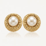 Paire de boucles d'oreilles rondes dorées, perle blanche nacrée au centre, cadre texturé.