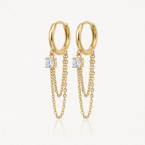 Paire de boucles d'oreilles créoles dorées avec chacune une pierre ronde brillante et deux chaînes fines pendantes.