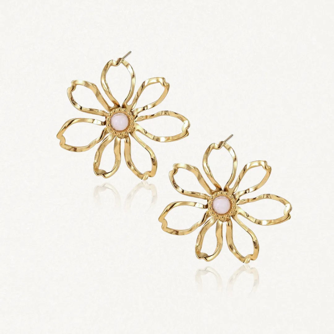 Deux boucles d'oreilles fleur en acier inoxydable doré avec des pétales ajourés et un cabochon central en nacre rose pâle.