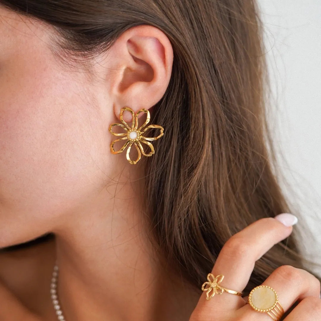 Boucle d'oreille fleur stylisée de 3cm en acier inoxydable doré avec centre en nacre, portée par une femme.