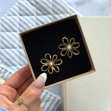 Deux boucles d'oreilles en acier inoxydable doré, en forme de fleurs texturées, avec un cœur en nacre blanche, dans une