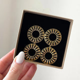 Main tient boîte cadeau avec 2 paires boucles d'oreilles dorées pendantes double cercle ajouré motif rayons sur velours noir.
