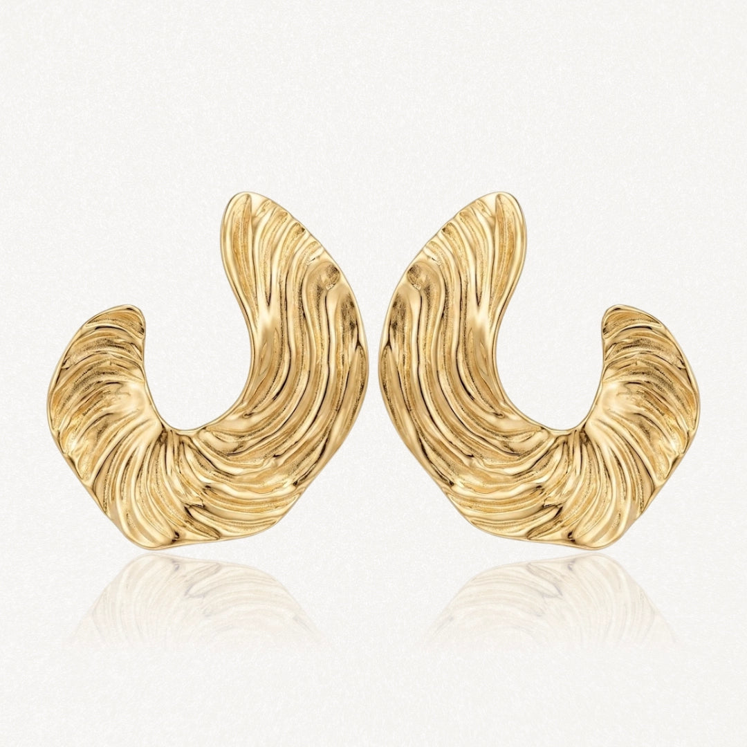 Paire de boucles d'oreilles dorées, épaisses et incurvées, avec une texture striée rappelant des vagues.
