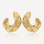 Paire de boucles d'oreilles dorées, épaisses et incurvées, avec une texture striée rappelant des vagues.