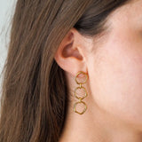 Oreille portant une boucle d'oreille en acier inoxydable doré, formée de trois anneaux irréguliers pendants.