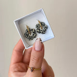 Boucles d'oreilles LENA en acier inoxydable doré avec un motif fleur blanc et noir dans une boîte blanche
