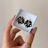 Boucles d'oreilles LENA en acier inoxydable doré avec motif de fleur noire à pois blancs dans une petite boîte blanche