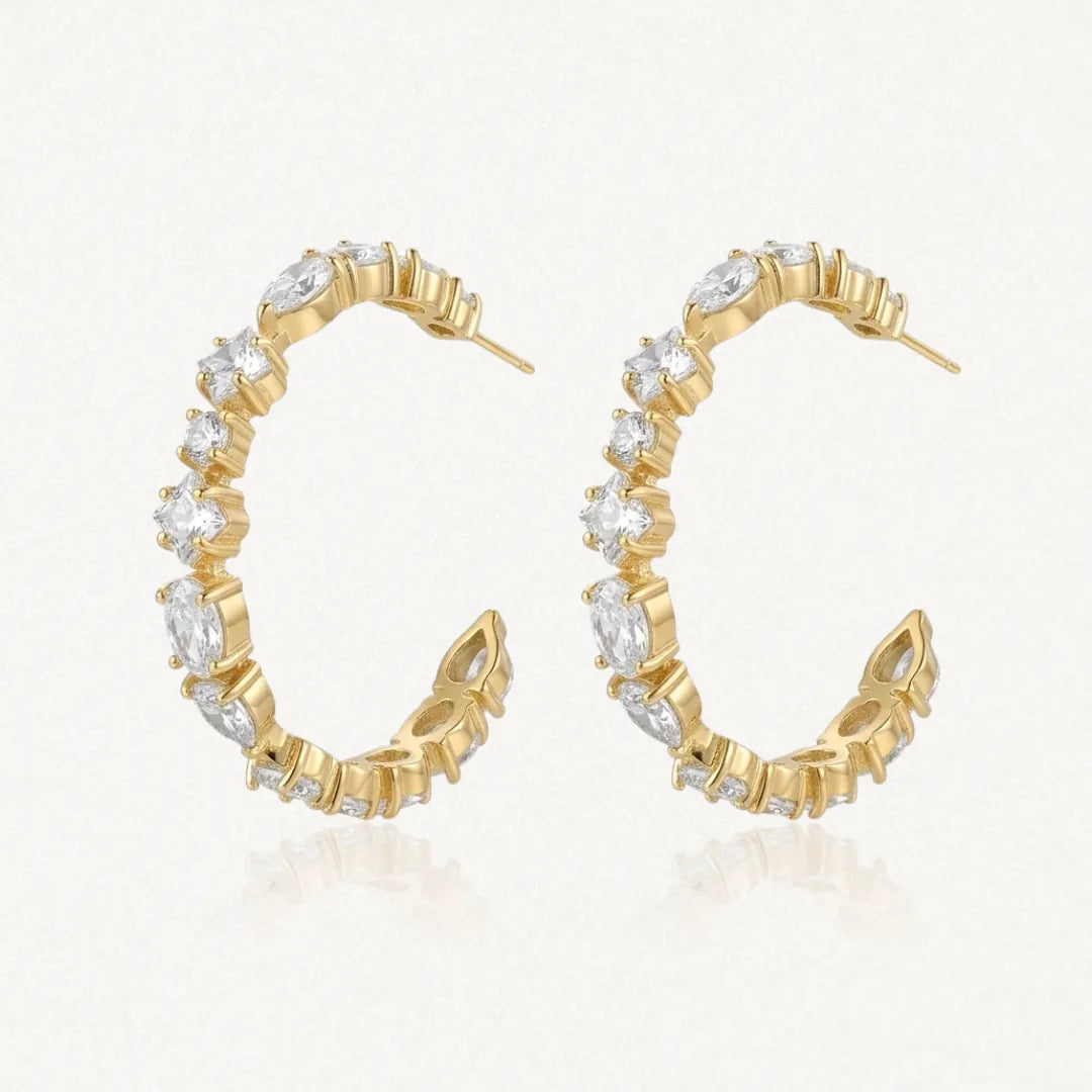 Deux boucles d'oreilles créoles tennis ovales en acier inoxydable doré, serties de zircons clairs de formes variées.