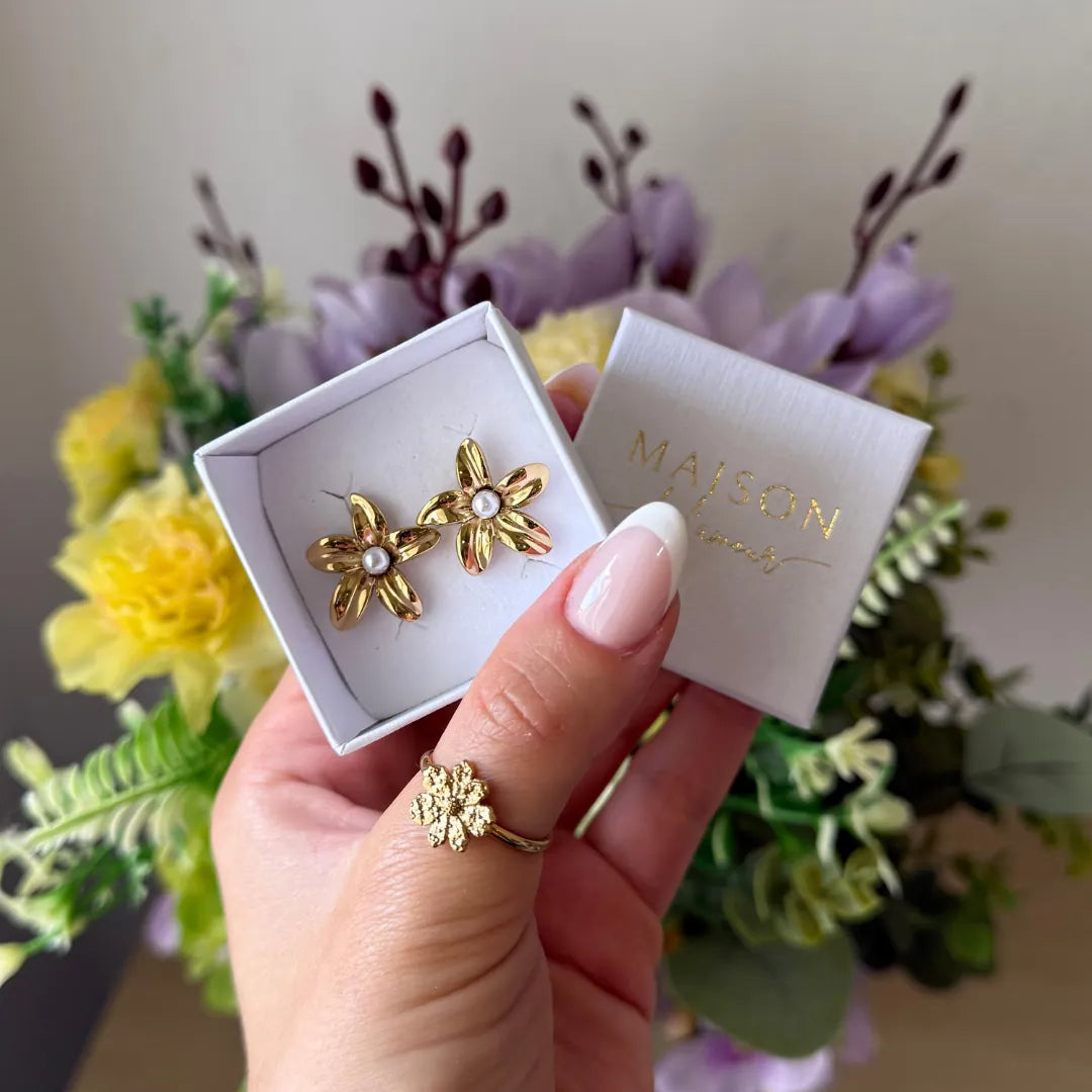 Boucles d'oreilles puces en acier inoxydable doré, en forme de fleurs avec une perle blanche. Elles sont dans un écrin blanc