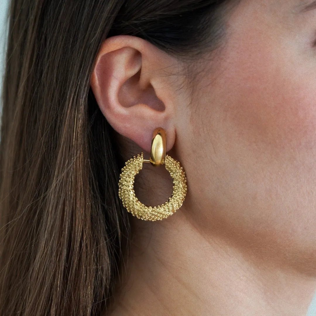 Boucle d'oreille dorée, grand anneau texturé granuleux sur le lobe d'oreille d'une femme.