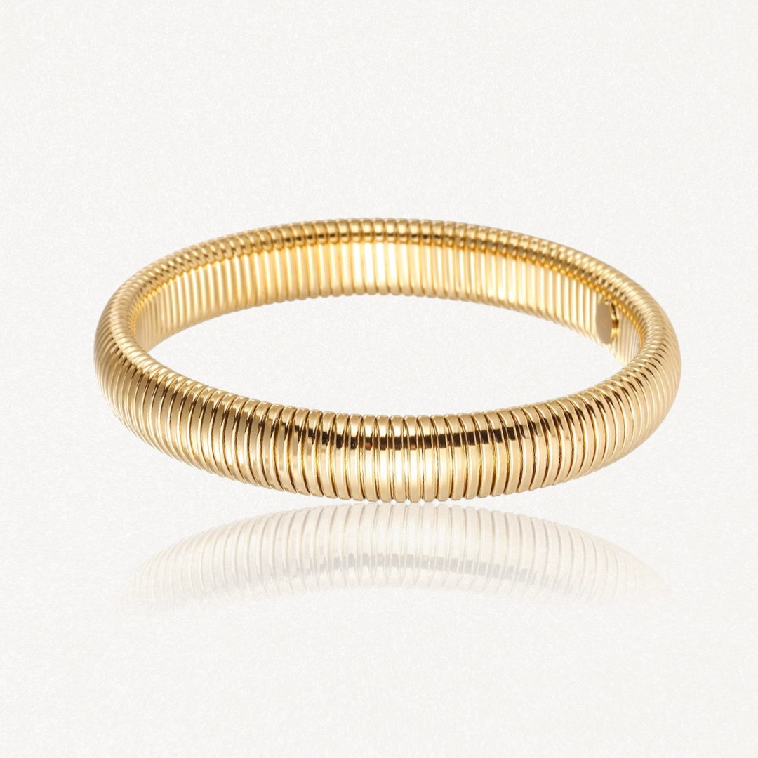 Bracelet doré, à la surface striée de fines nervures parallèles serrées, reflétant la lumière sur un fond blanc.