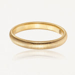 Bracelet doré, à la surface striée de fines nervures parallèles serrées, reflétant la lumière sur un fond blanc.