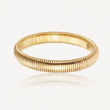 Bracelet doré, à la surface striée de fines nervures parallèles serrées, reflétant la lumière sur un fond blanc.