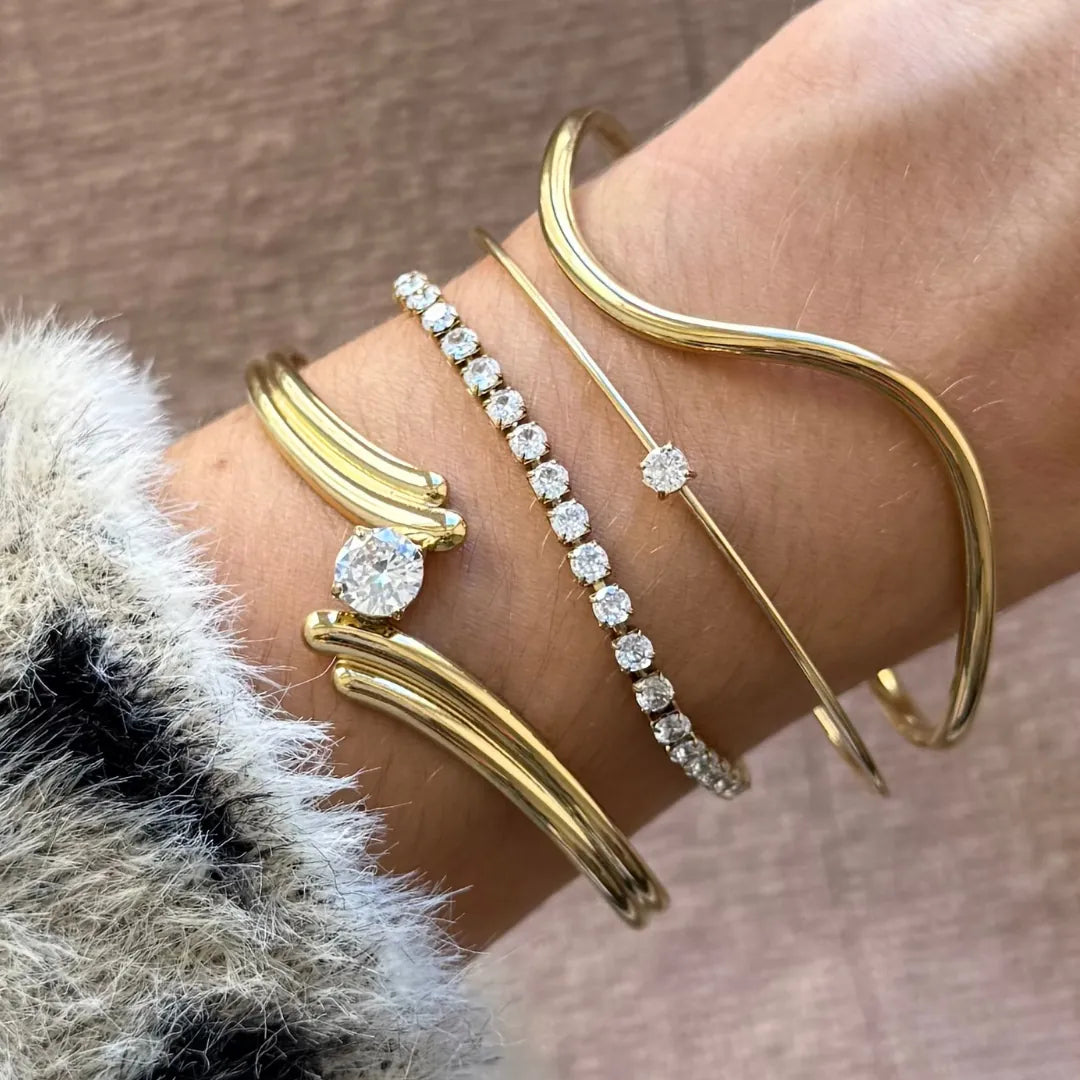 Poignet portant un jonc ouvert croisé multirang en acier inoxydable doré à zircon, et 3 autres bracelets dorés dont certains