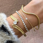Poignet portant un jonc ouvert croisé multirang en acier inoxydable doré à zircon, et 3 autres bracelets dorés dont certains