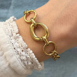 Bracelet à maillons dorés alternant ovales lisses et ronds martelés au poignet, avec manche en dentelle blanche.