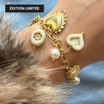 Bracelet à charms dorés et blancs porté au poignet avec mention Édition Limitée, associé à un vêtement en fausse fourrure.