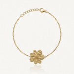 Bracelet fin en acier inoxydable doré avec un pendentif fleur texturé et une chaînette réglable.