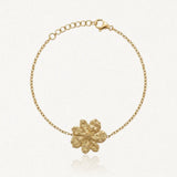 Bracelet fin en acier inoxydable doré avec un pendentif fleur texturé et une chaînette réglable.