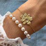Poignet avec deux bracelets. Un bracelet en acier inoxydable doré avec une fleur texturée. L'autre bracelet est une rangée de