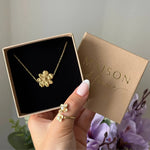 Bracelet en acier inoxydable doré à pendentif fleur texturée, présenté dans un écrin. Une bague assortie avec perles est au