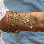 Bras de femme. Quatre bracelets en acier inoxydable dore a motifs fleurs. Un large ajoure, trois fins a pendentifs fleurs
