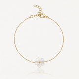 Bracelet en chaîne dorée avec petites perles blanches et un pendentif fleur en nacre à cinq pétales, centre doré. Fermoir