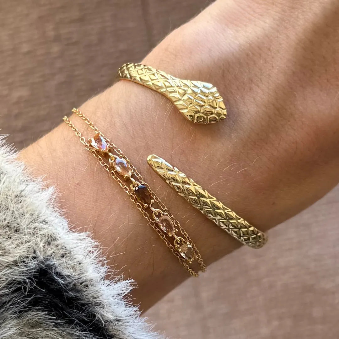 Bracelet double chaîne acier inoxydable doré, zircons champagne et marron, au poignet avec un jonc serpent doré.