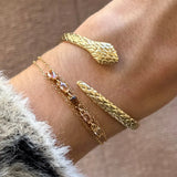 Bracelet double chaîne acier inoxydable doré, zircons champagne et marron, au poignet avec un jonc serpent doré.