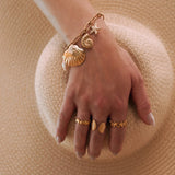 Bracelet en acier inoxydable doré avec charmes coquillages et étoile de mer sur une main de femme.