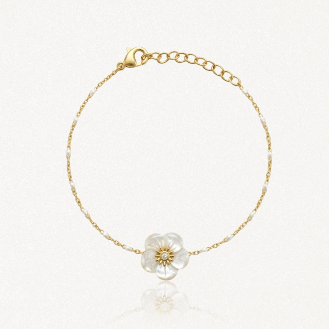 Bracelet chaîne fine dorée agrémentée de perles blanches. Fleur en nacre avec diamant. Fermoir mousqueton doré.
