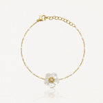 Bracelet chaîne fine dorée agrémentée de perles blanches. Fleur en nacre avec diamant. Fermoir mousqueton doré.