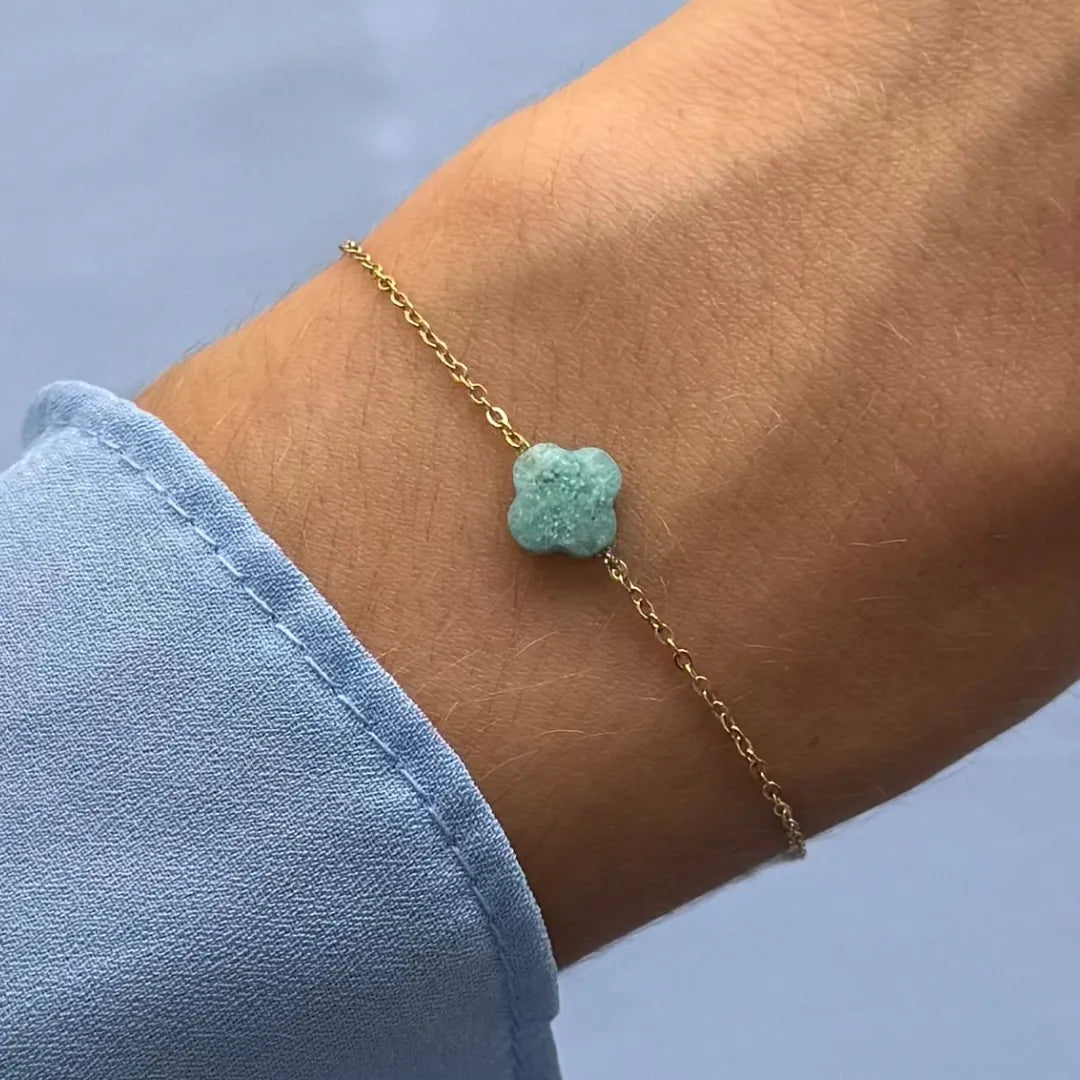 Bracelet fin en acier inoxydable doré, avec un trèfle en amazonite verte texturée, porté sur un poignet.