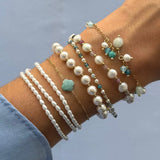 Un poignet avec une superposition de bracelets en acier inoxydable doré. Ils sont ornés de perles blanches, d'amazonite et de
