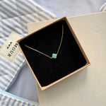 Bracelet fin trèfle en acier inoxydable doré et amazonite, présenté dans un écrin beige à l'intérieur noir.